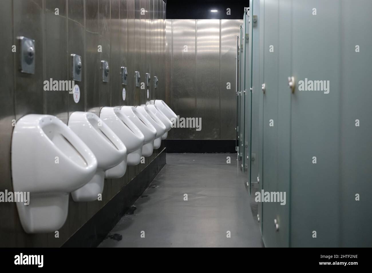Public men's toilets lined up on the wall facing toilets with doors