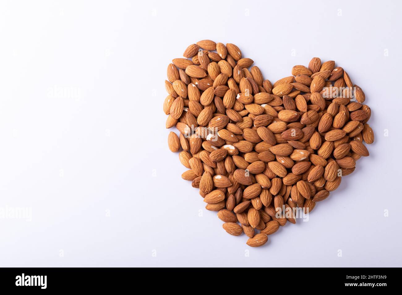 High angle close-up of almonds arranged in heart shape pattern on wooden white background Stock Photo