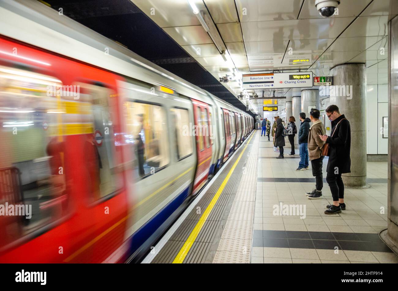 Passengers standing, waiting on a platform at Embankment London Underground Station as a train arrives. Stock Photo