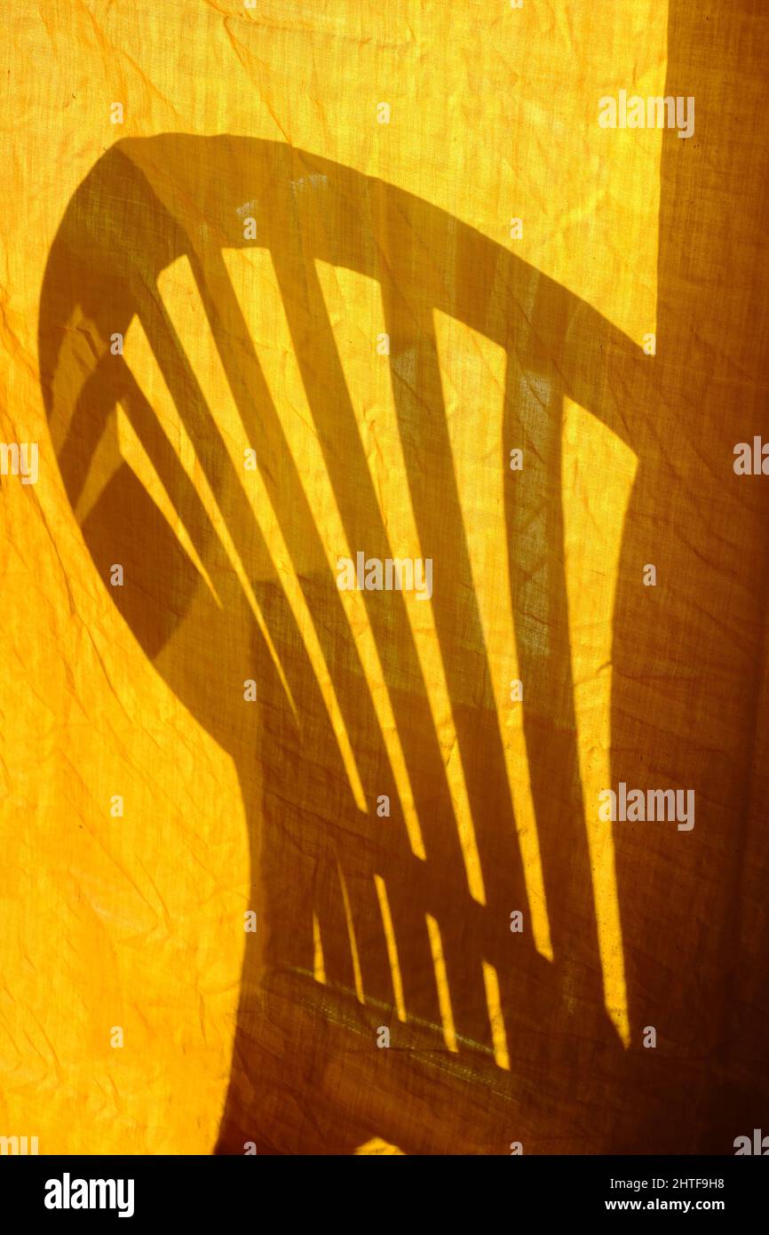 Shadow of a garden chair on a old hanging orange bedsheet Stock Photo