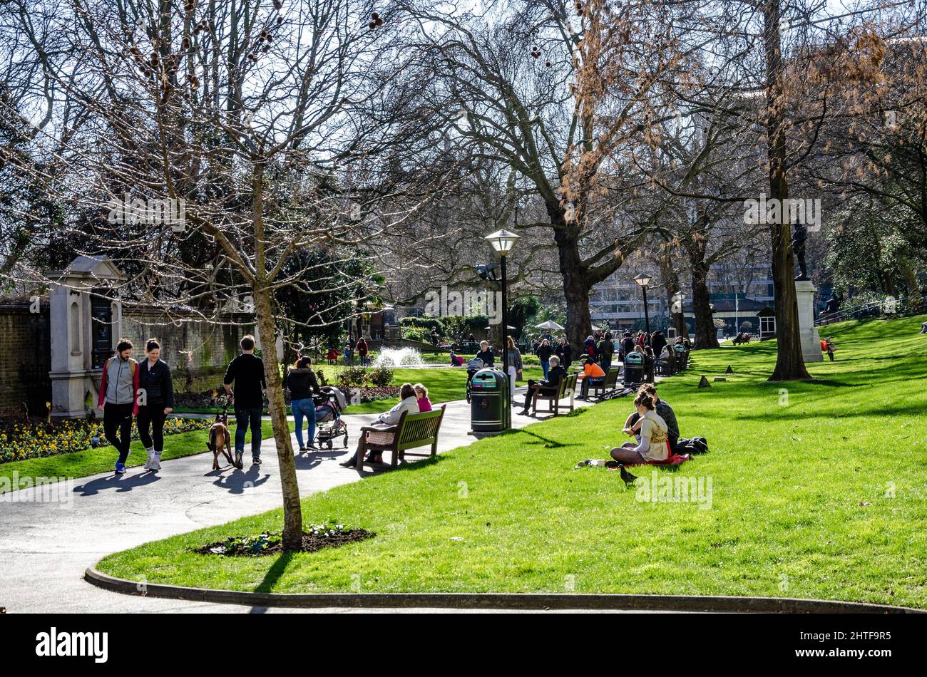 London Memorial Gardens busy with people walking and sat on benches along the main path through the park. Stock Photo