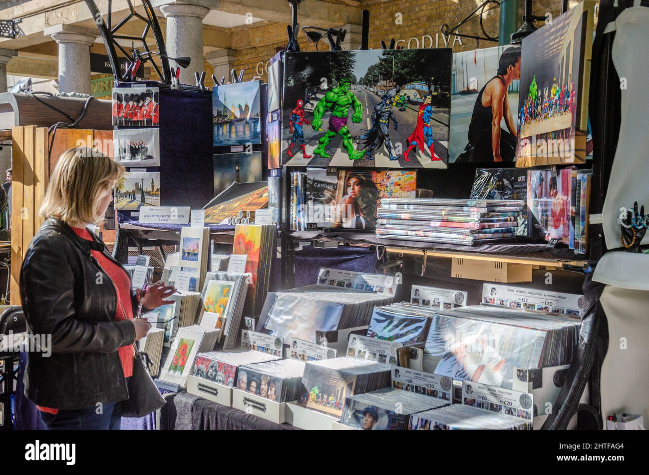 A woman browsing the prints and artwork on display at a stall in The Apple Market in Covent Garden, London, UK Stock Photo
