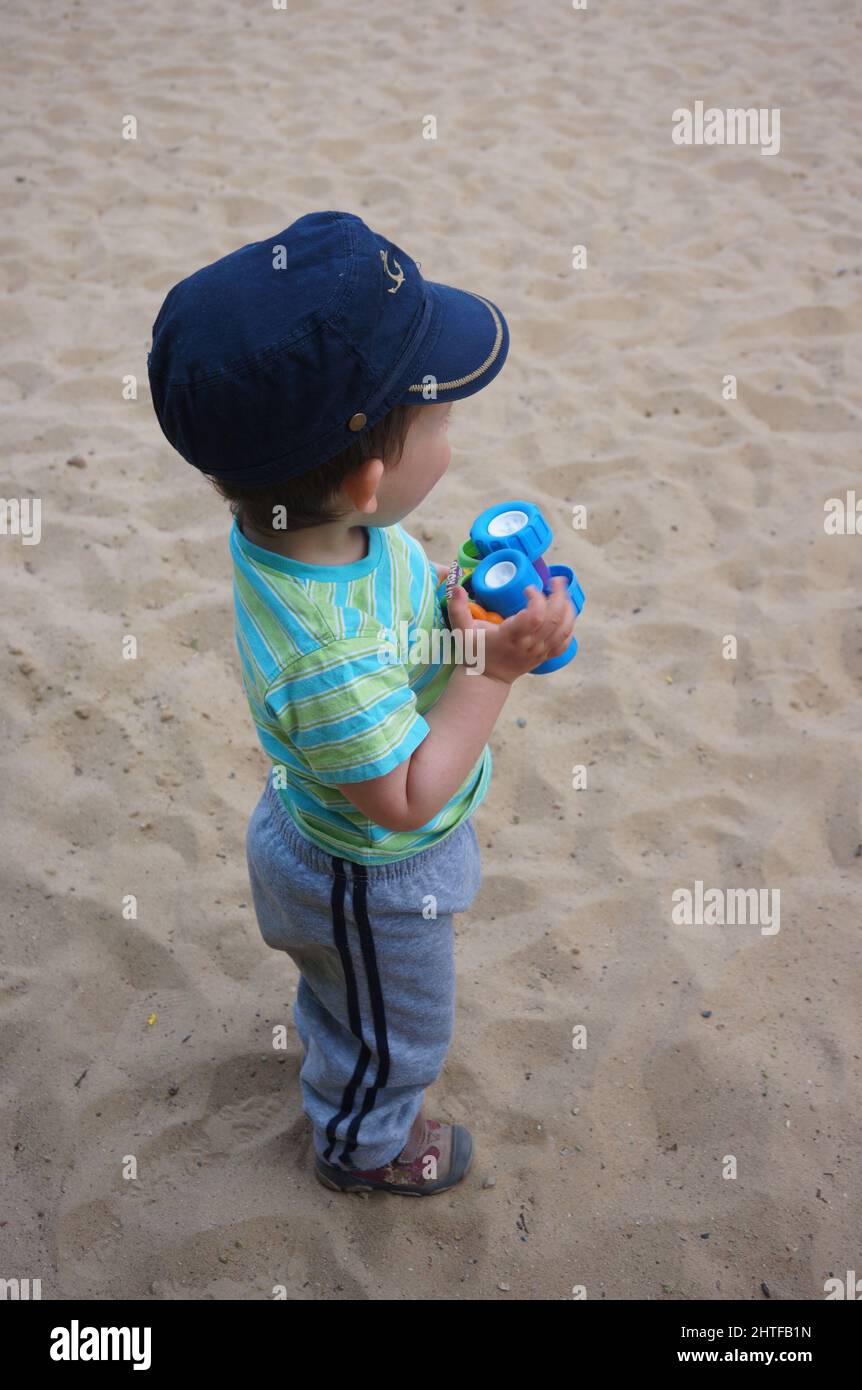 A Young boy holding a plastic toy car while standing on sand Stock Photo