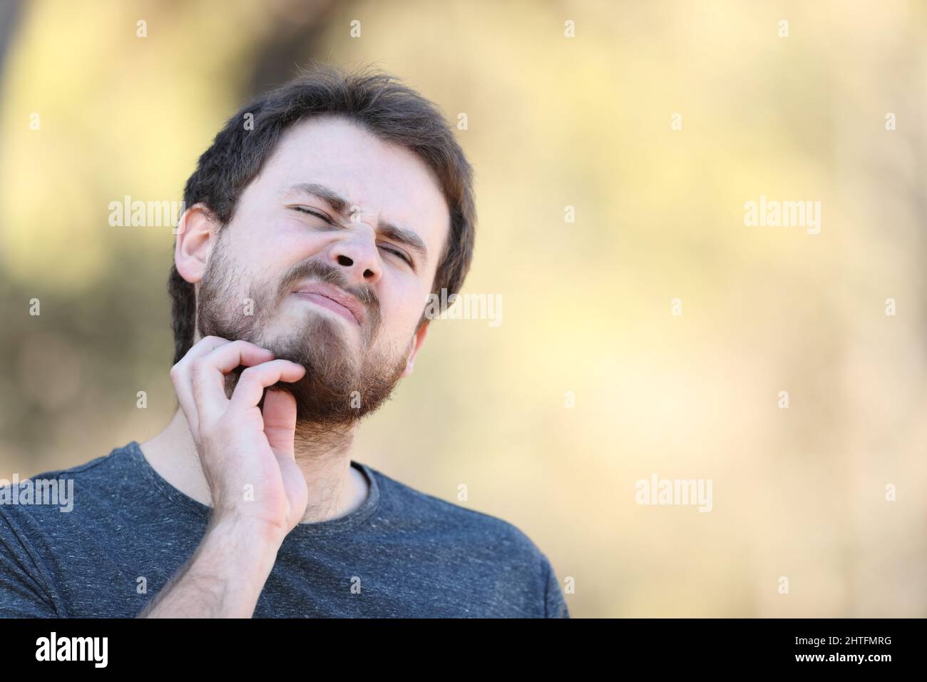 Overwhelmed man scratching itchy beard outdoors Stock Photo