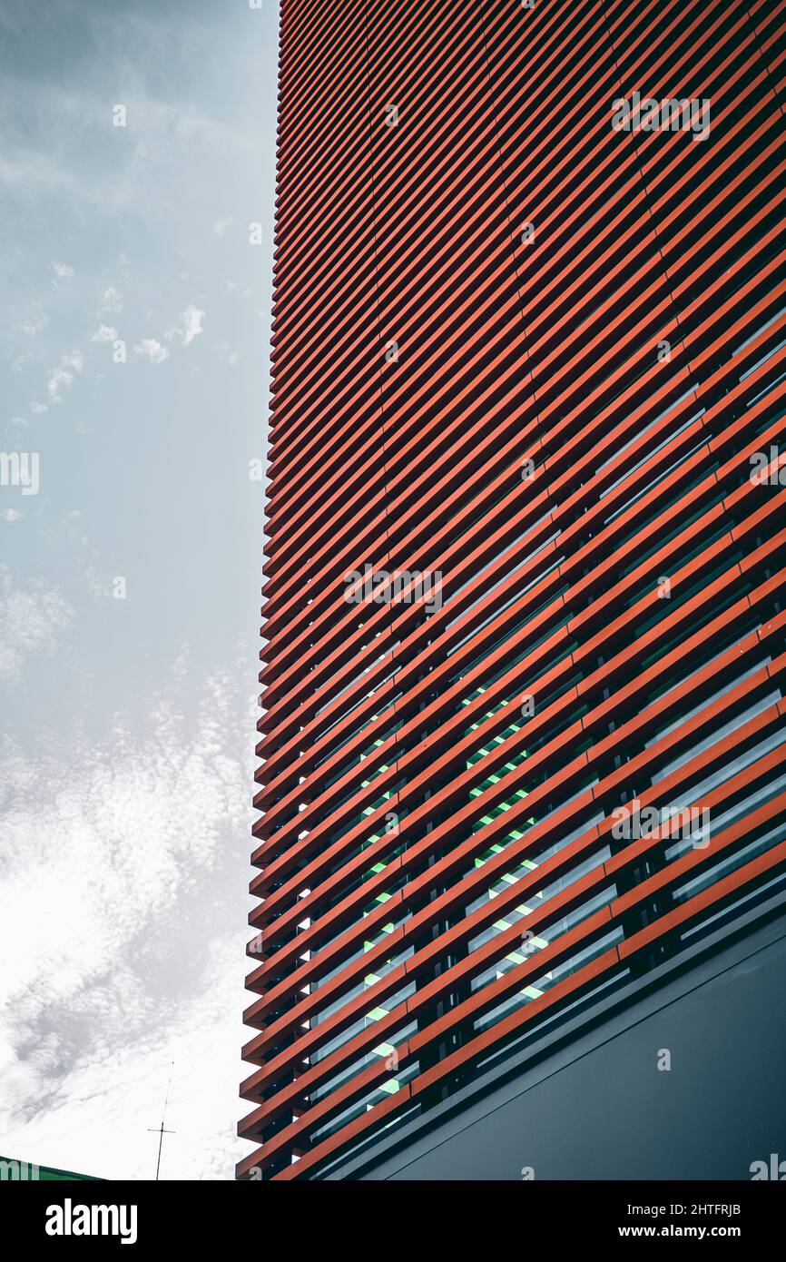 Low angle shot of a tall modern building in a red facade under a cloudy ...