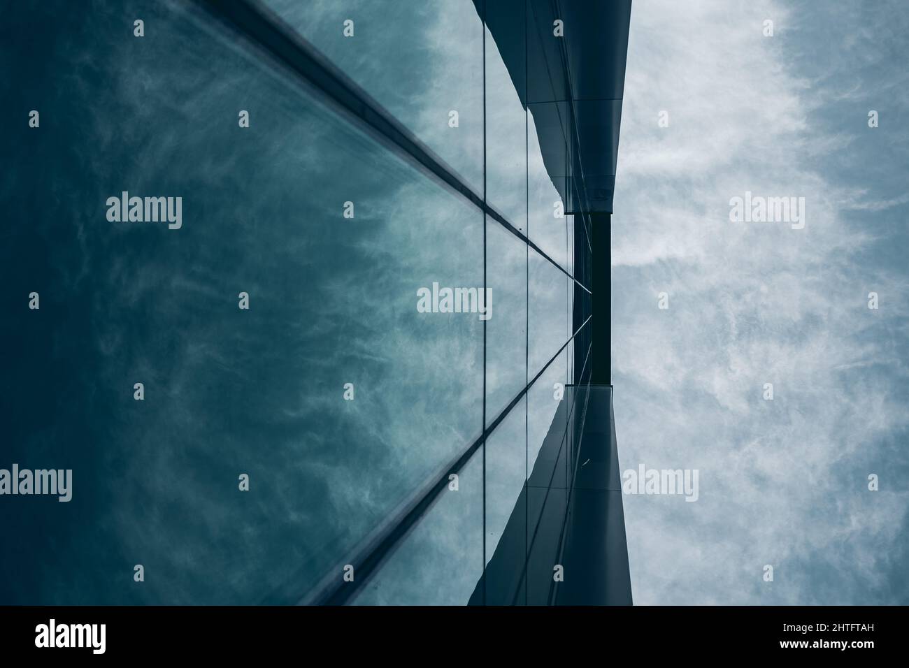 Low angle shot of a tall building in a glass facade under a cloudy sky ...