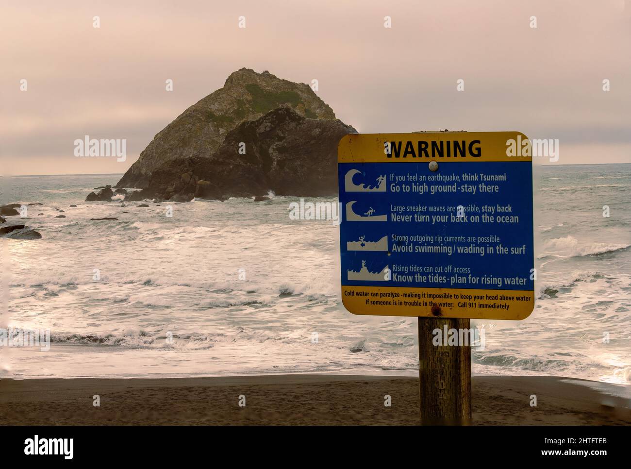 A sign on the California Pacific coast warns of tsunami dangers should an earthquake occur and gives safety instructions. Stock Photo