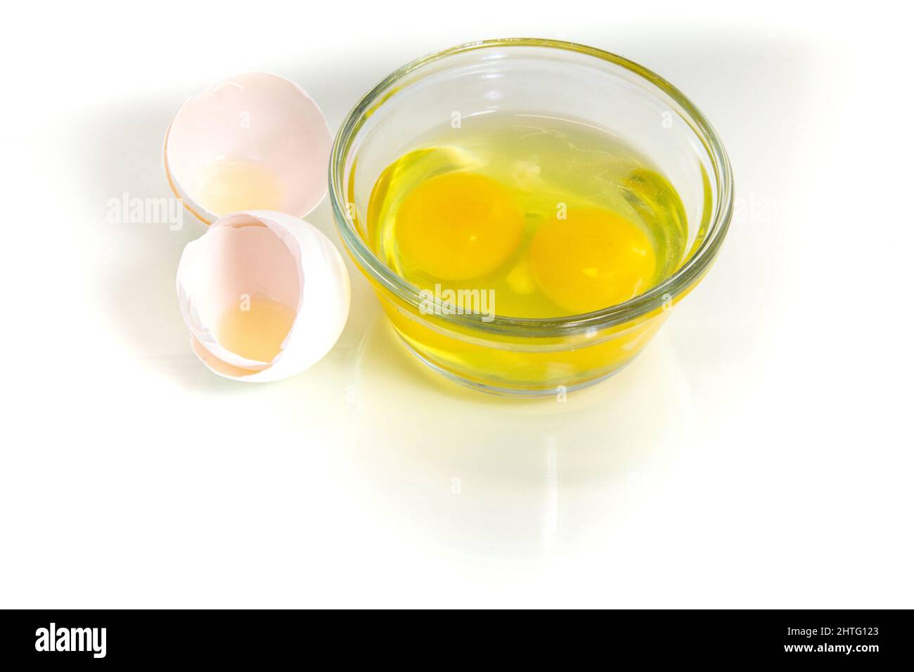 Two fresh broken eggs in a glass bowl with broken shell near. Studio