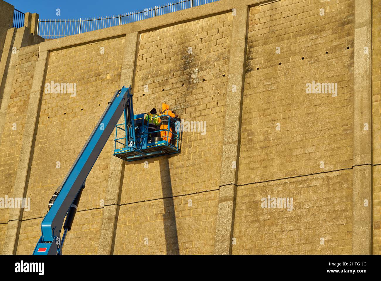 Men repair a high cliff wall on articulated arm Stock Photo