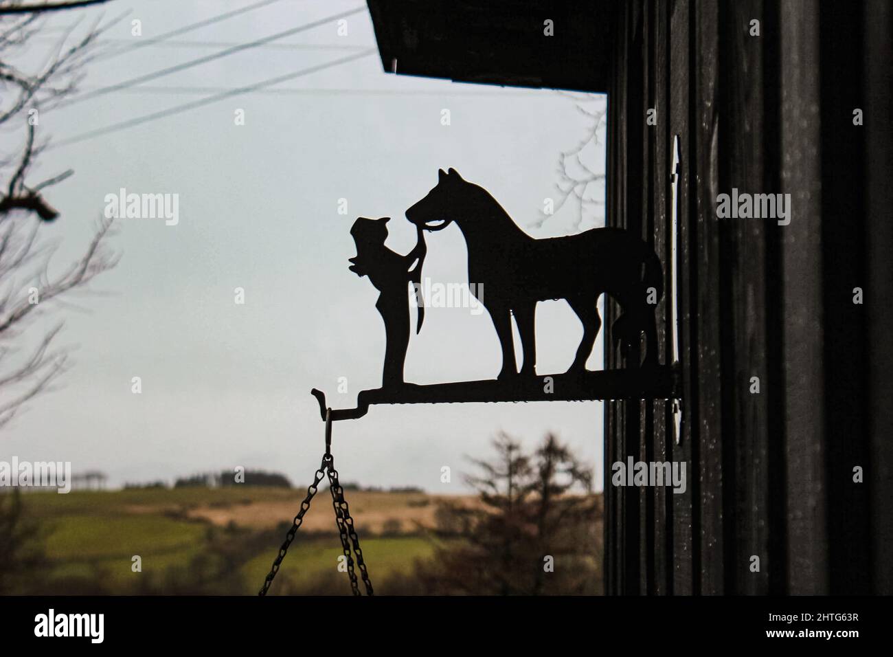 Artistic black hanging basket hook depicting a woman and a horse in front of views of the Ceredigion hills in Cwmann, Wales Stock Photo