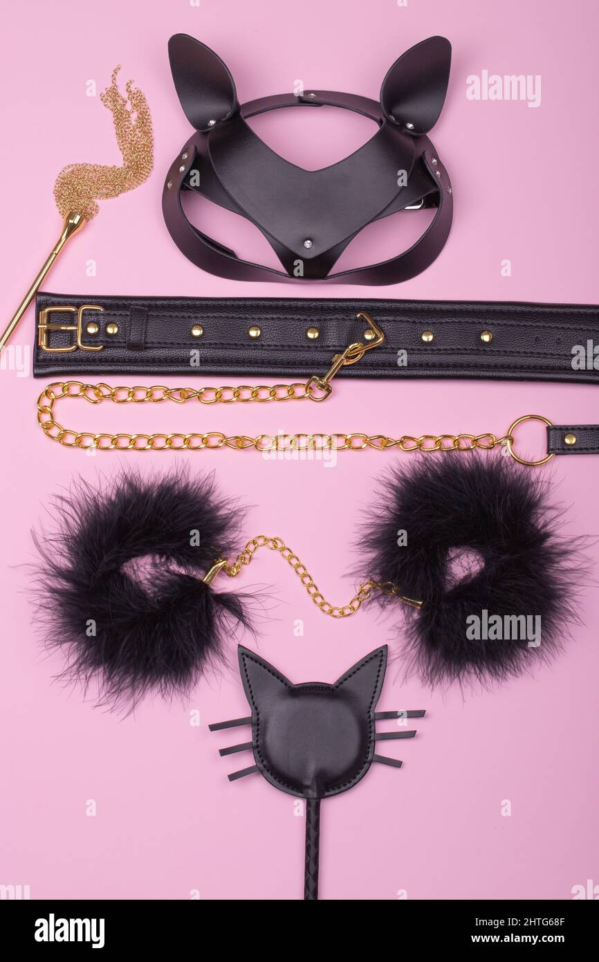 Set of erotic toys for BDSM. The game of sexual slavery with a whip, handcuffs, leather leash and mask on a light pink background. Intimate sex games. Stock Photo