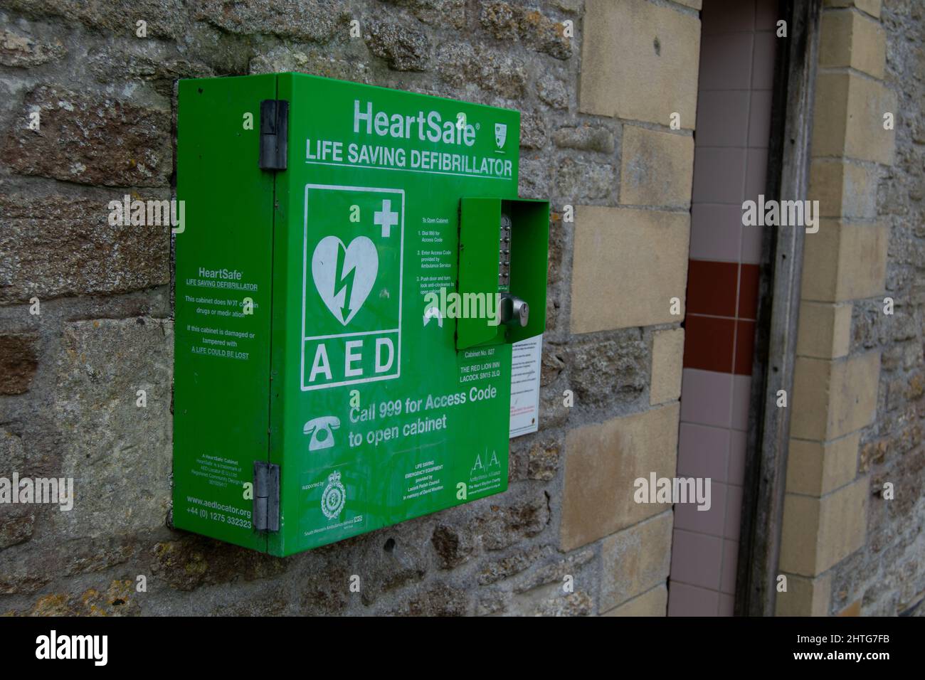 Lacock,UK-Sept 2021: Green defibrillator cabinet seen from the left, fixed onto the building wall for anybody to use in case of emergency, life saving Stock Photo