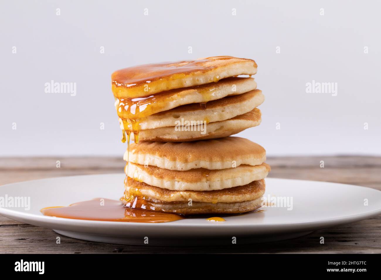 Stack of eight pancakes with syrup served in plate on table against gray background Stock Photo
