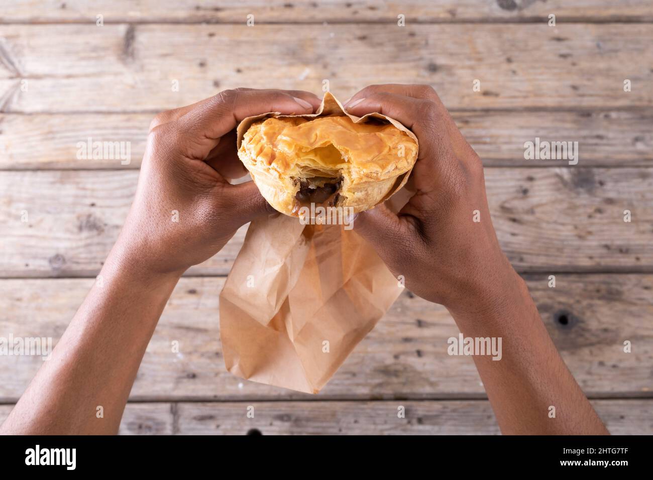 Cropped hands of african american male holding stuffed pie with missing bite over table Stock Photo