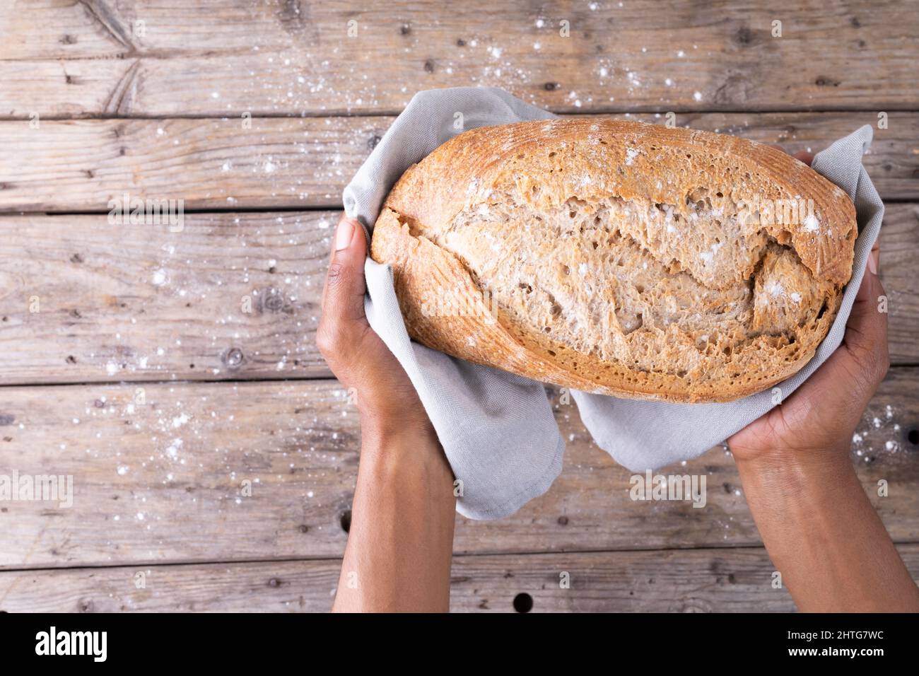 Overhead view of cropped african american male hands holding baked bread loaf over table Stock Photo