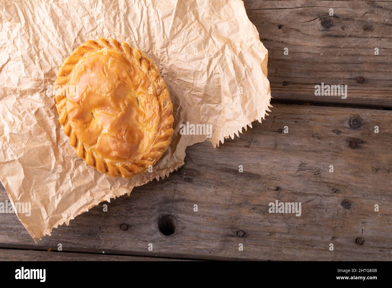 Directly above shot of baked stuffed pie on brown wax paper over wooden table Stock Photo