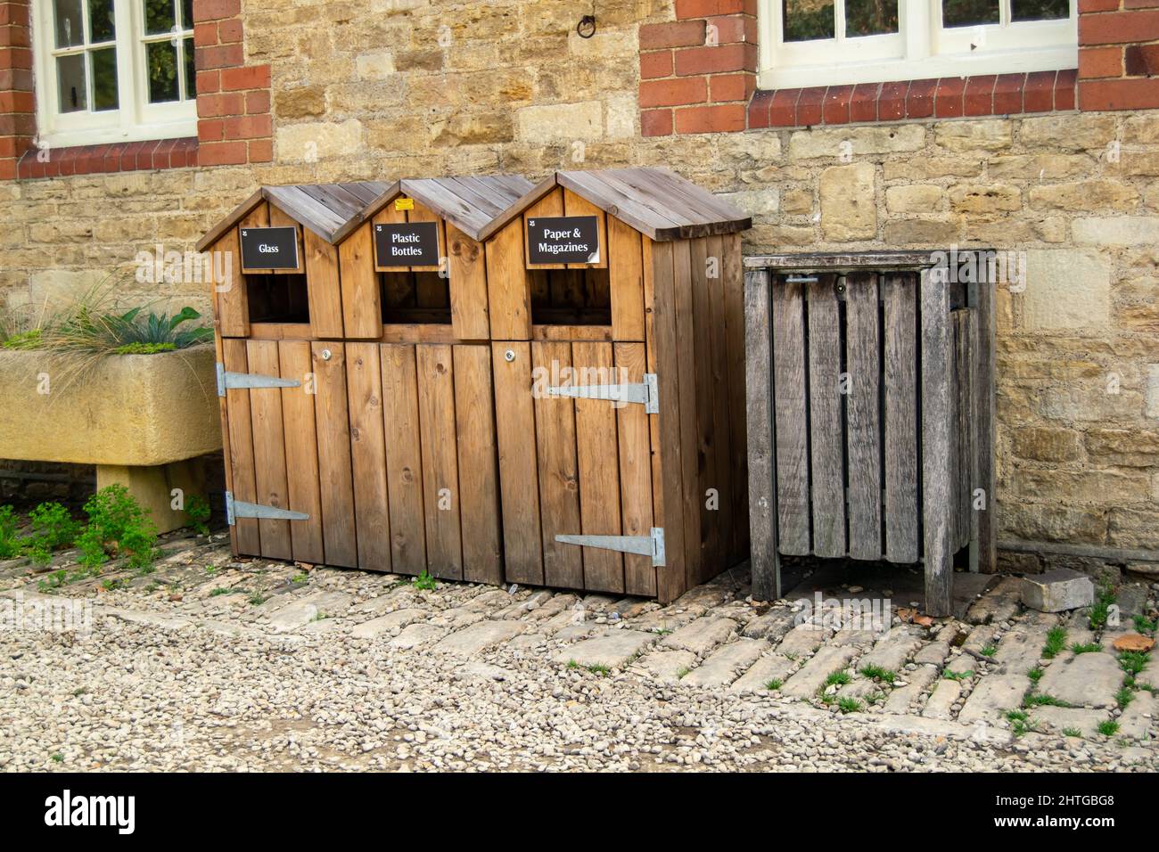 Three wooden recycling bins with non recycling waste bin next to them. Paper, magazines, glass and plastic bottles recycle units standing by the Stock Photo