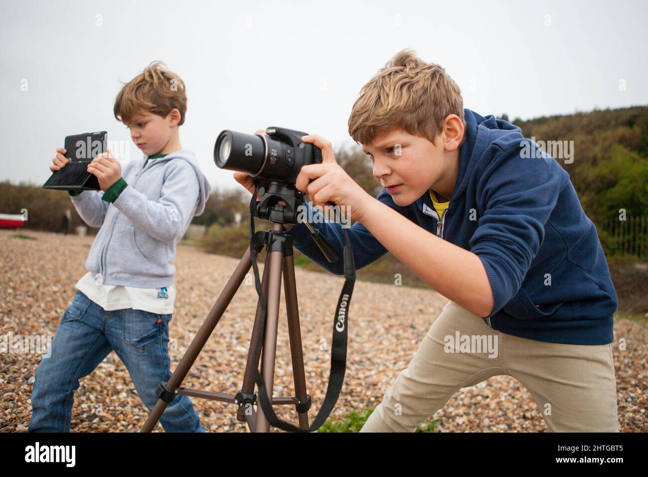 A young teenage boy takes a photograph with a Canon camera mounted on a tripod Stock Photo