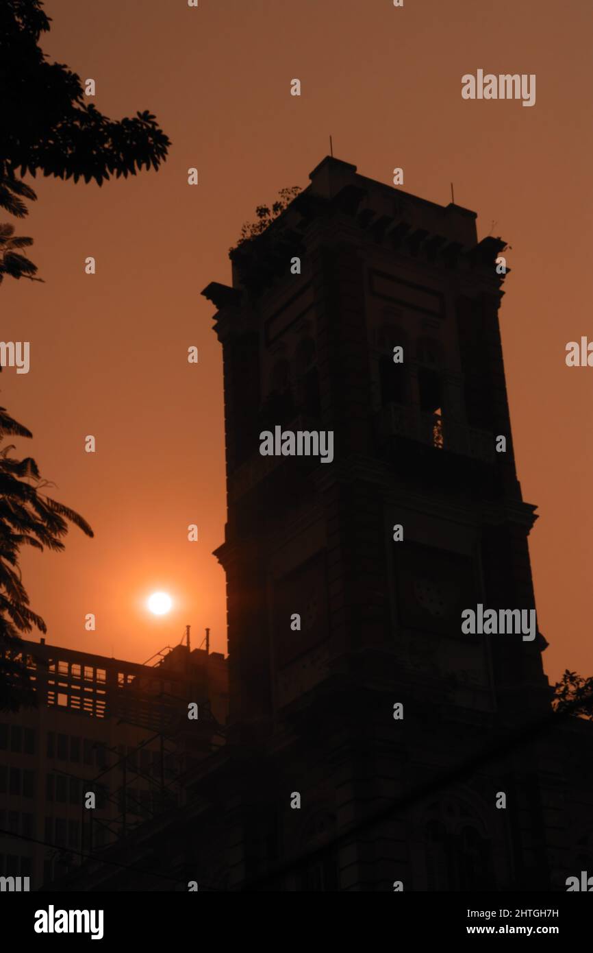 Silhouette of a building tower in dusk time sun setting with orange sky ...