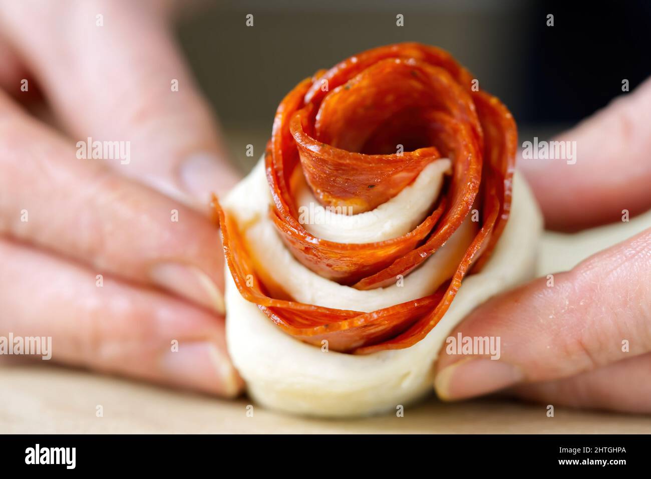 woman is making roseshaped pepperoni snack. pastry with salami