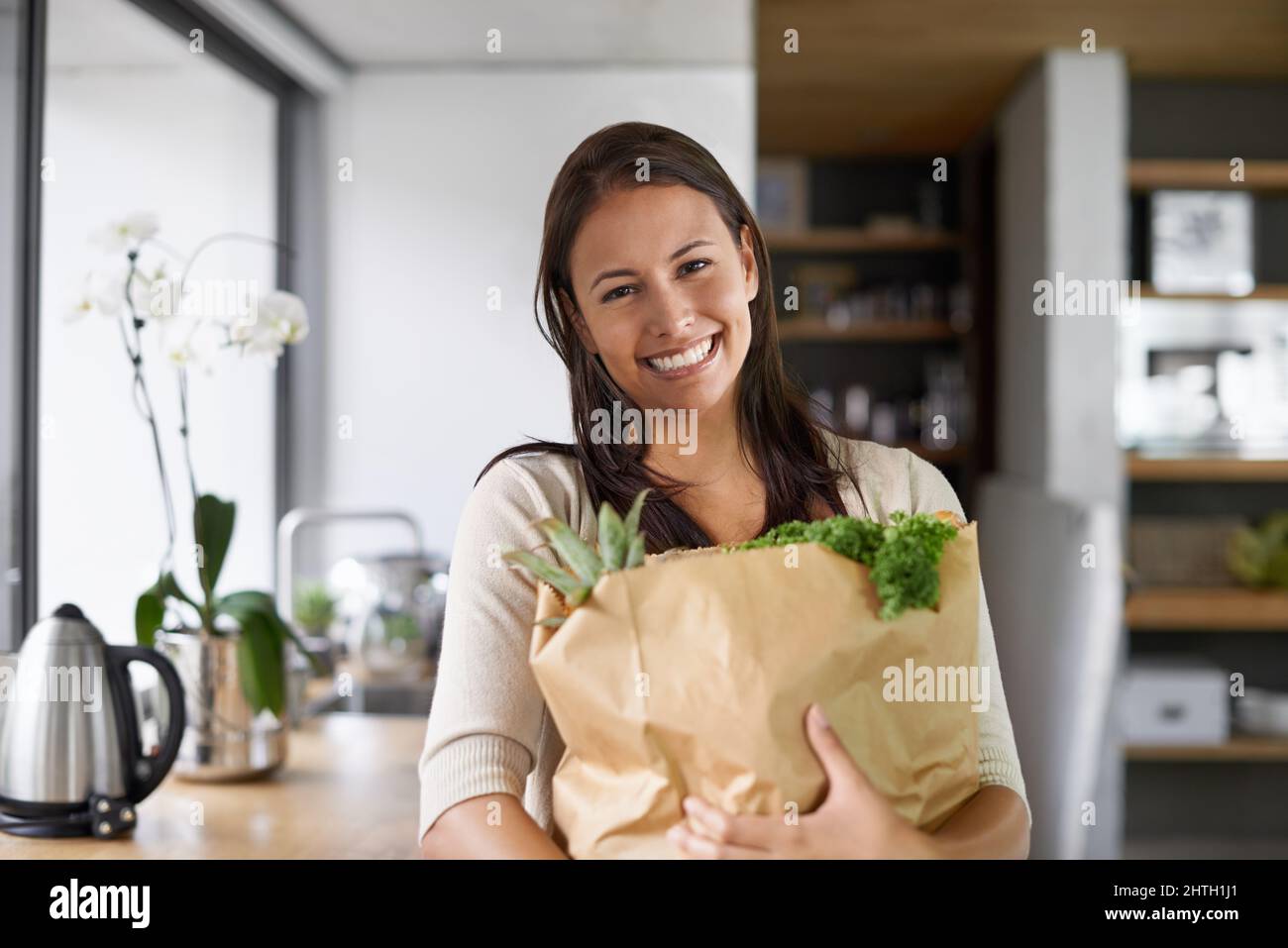 I only buy organic. A young woman standing in her kitchen holding a bag of groceries - portrait. Stock Photo