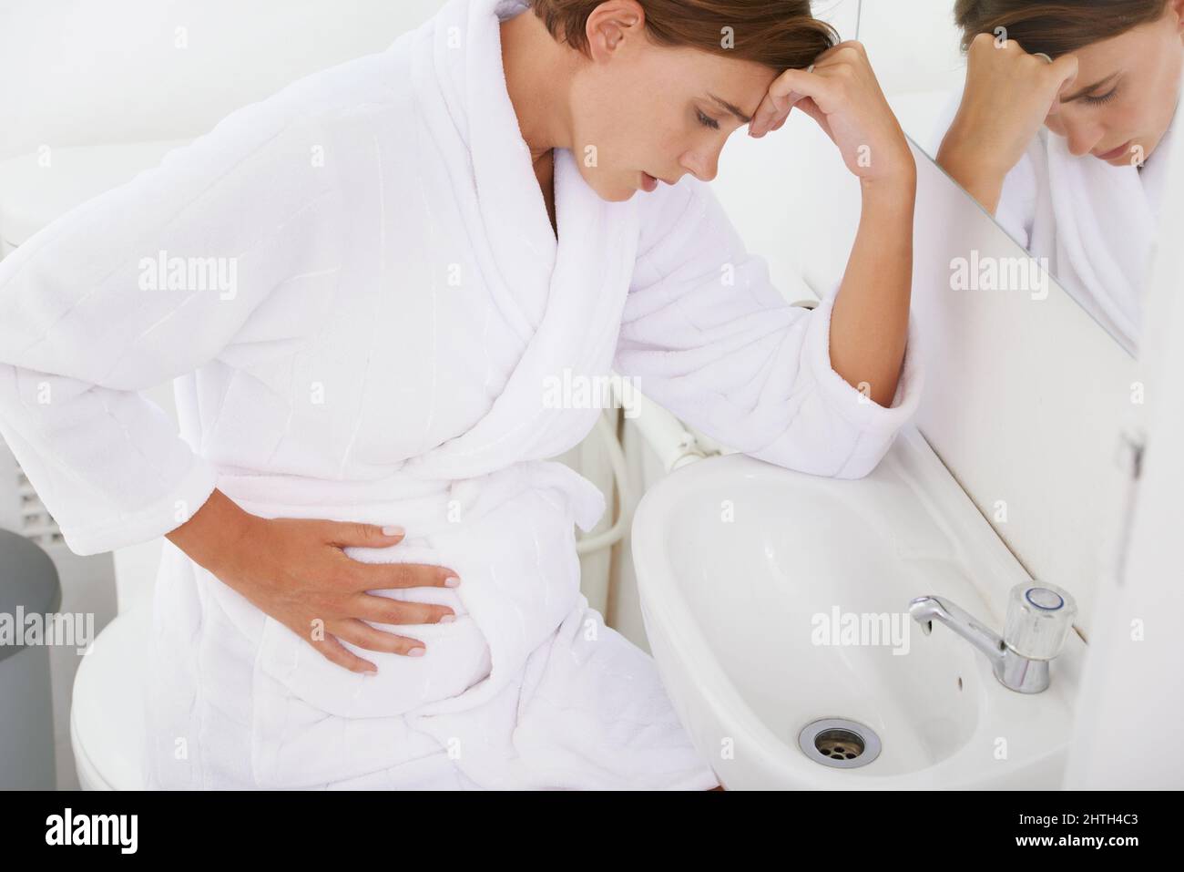 Struggling with morning sickness. A pregnant woman struggling with morning sickness in the bathroom. Stock Photo