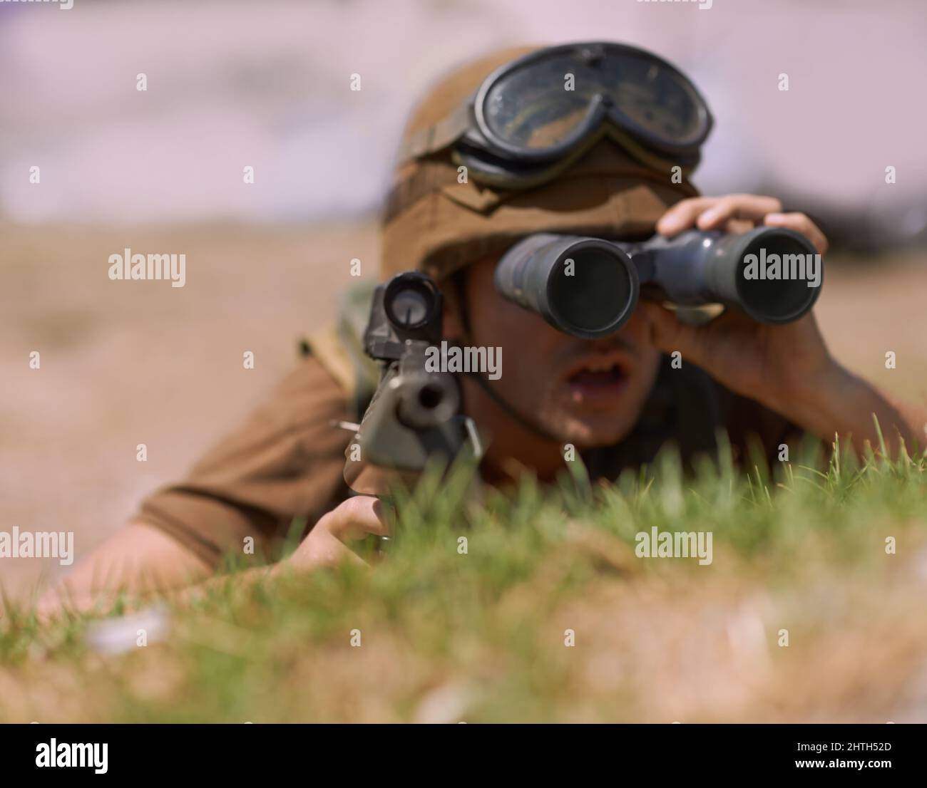 The enemy is in sight. A young soldier looking through his binoculars. Stock Photo