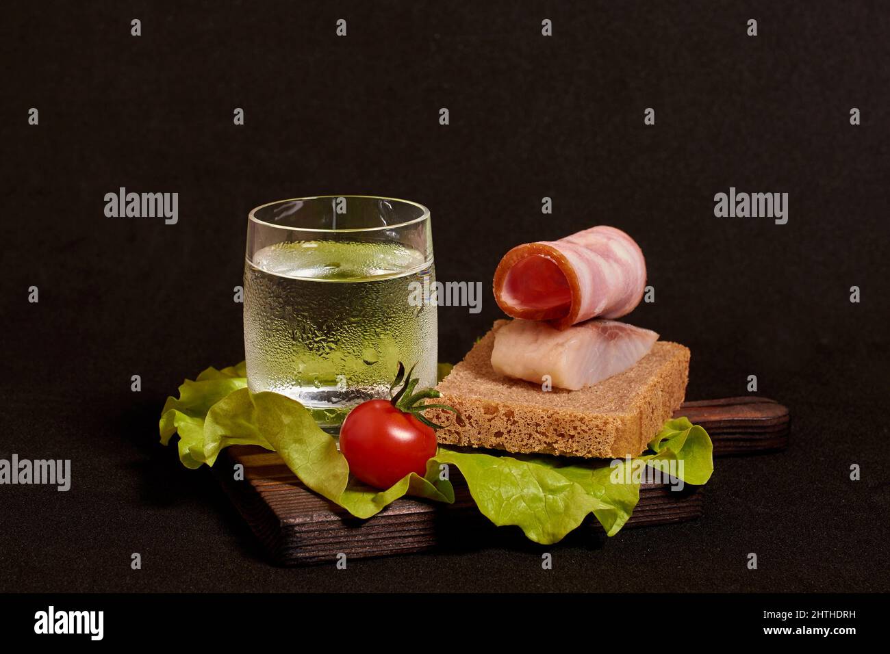 A glass of vodka, a sandwich with rye bread, herring and ham and tomato, lettuce Stock Photo