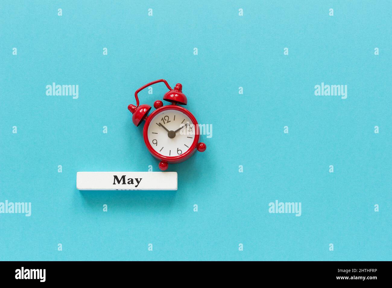 Wooden calendar spring month May and red alarm clock on blue paper background. Concept Hello May or Good bye May Creative Top view Flat Lay Minimal st Stock Photo