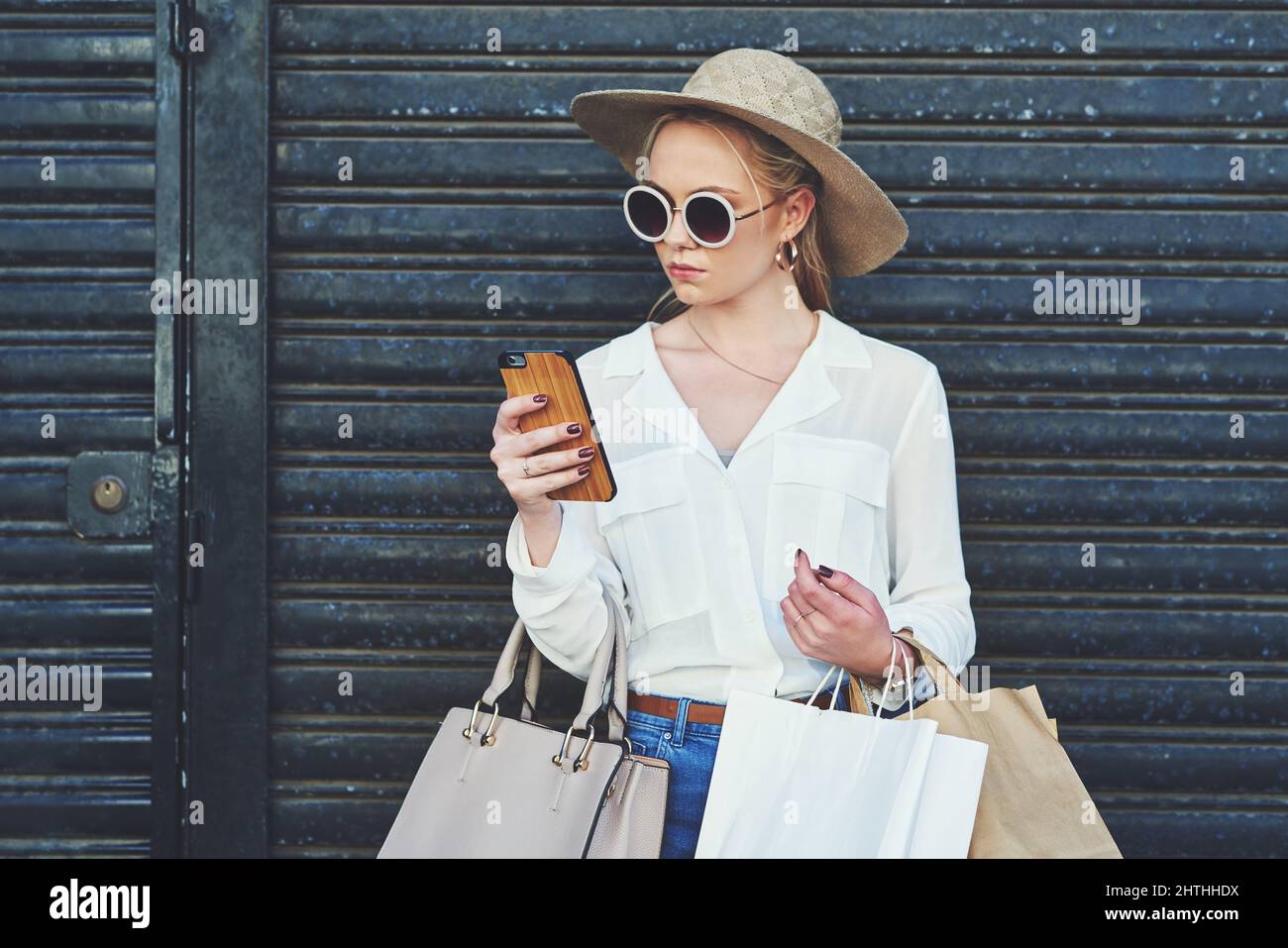 https://c8.alamy.com/comp/2HTHHDX/her-friends-have-to-hear-about-todays-deals-cropped-shot-of-an-attractive-young-woman-using-a-smartphone-while-holding-shopping-bags-against-an-urban-2HTHHDX.jpg