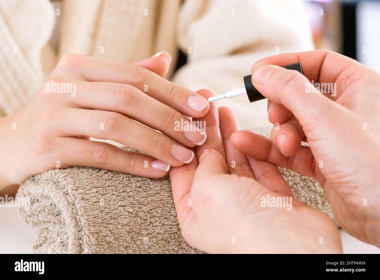 Crop anonymous manicure master applying nail polish to customer in bathrobe during beauty procedure in salon Stock Photo