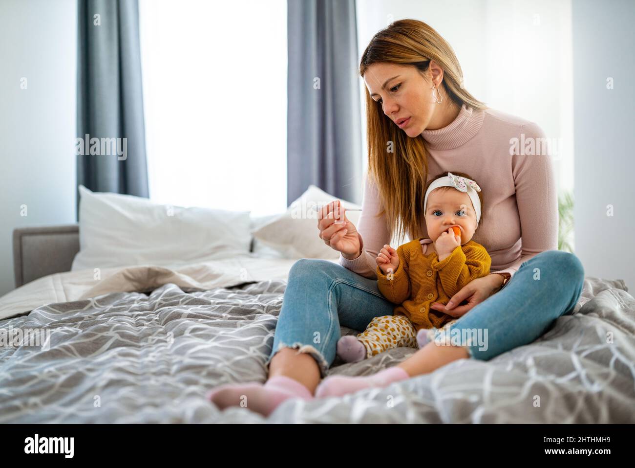 Mother measuring temperature of her ill kid. Sick child with high fever, mother holding thermometer. Stock Photo