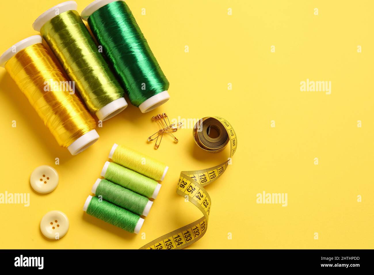 Thread spools, buttons and measuring tape on yellow background Stock Photo