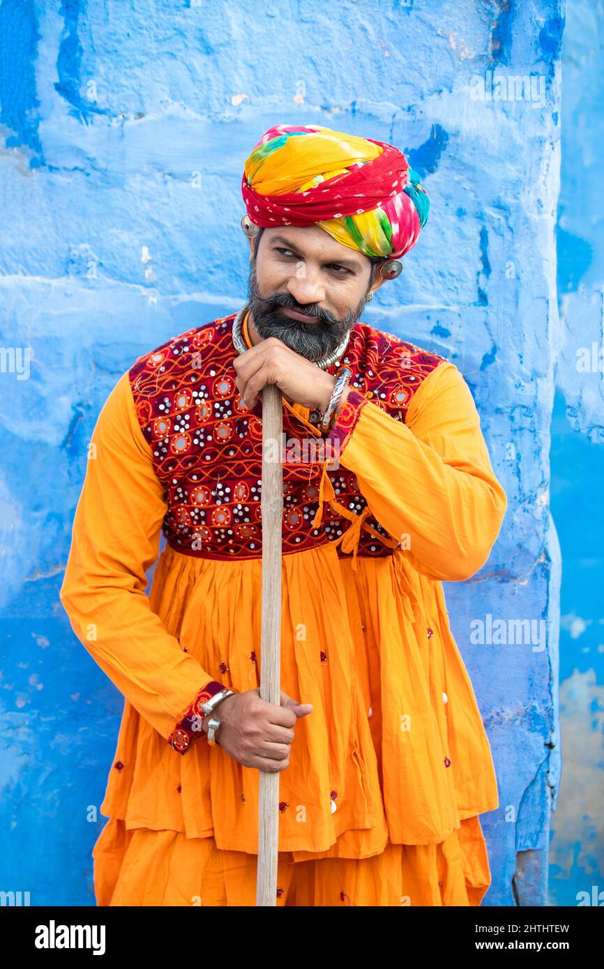 Happy traditional north indian man wearing colorful attire holding wood stick. Rajasthan male with turban and ethnic outfits. Culture and fashion. Stock Photo