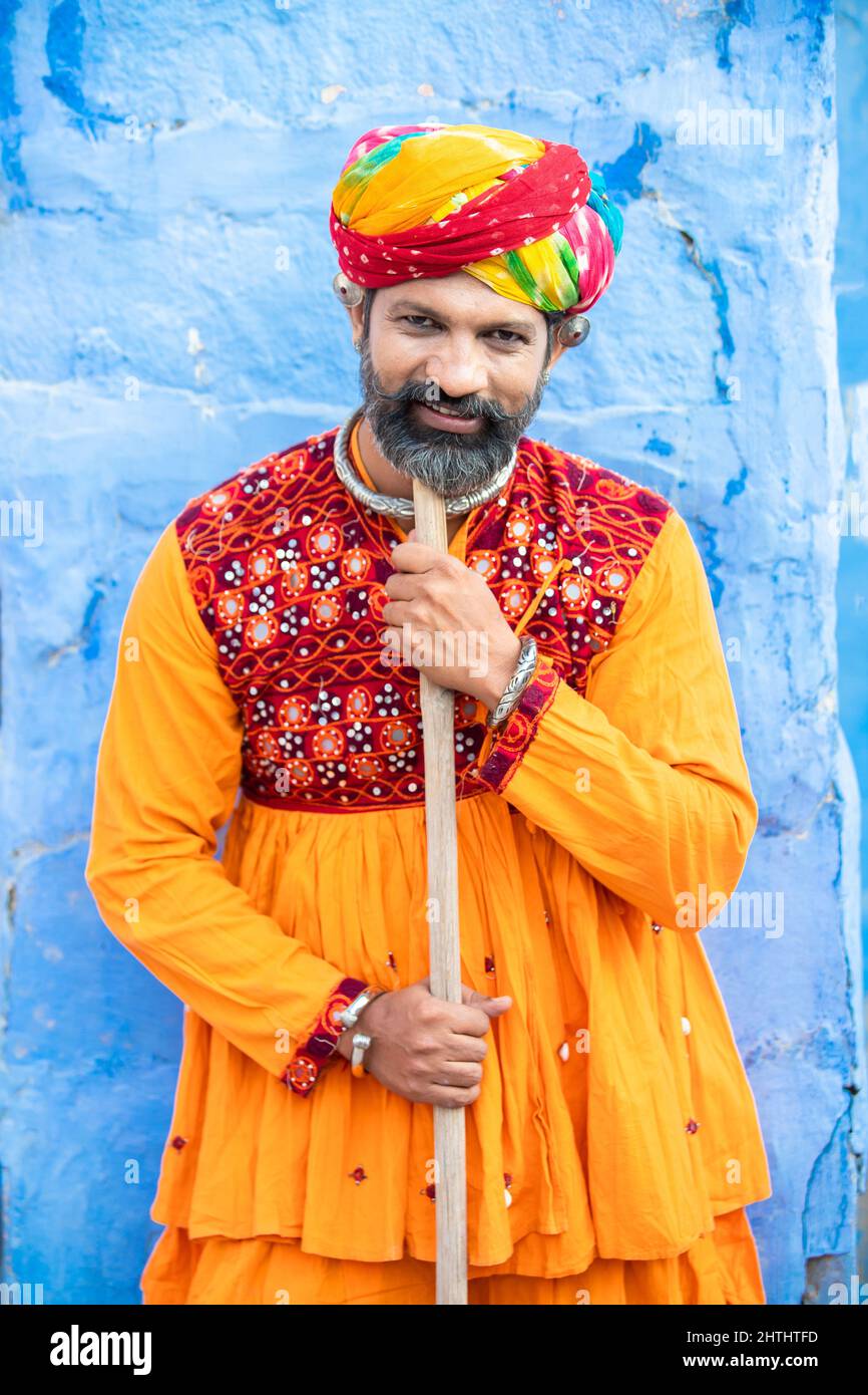 Happy traditional north indian man wearing colorful attire holding wood stick. Rajasthan male with turban and ethnic outfits. Culture and fashion. Stock Photo
