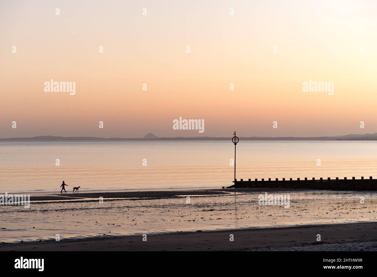 Edinburgh, Scotland, UK, 1st March 2022. UK Weather: Edinburgh wakes up to a sunny morning. A person walking a dog along the beach in Portobello. Credit: Lorenzo Dalberto/Alamy Live News Stock Photo