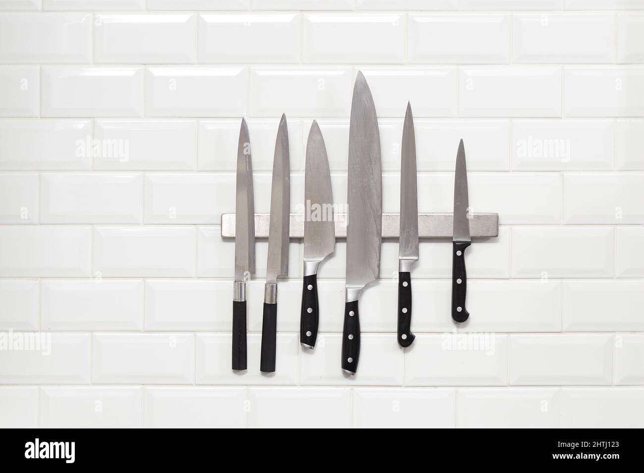 Six Japanese knifes hanging on white wall tile Stock Photo