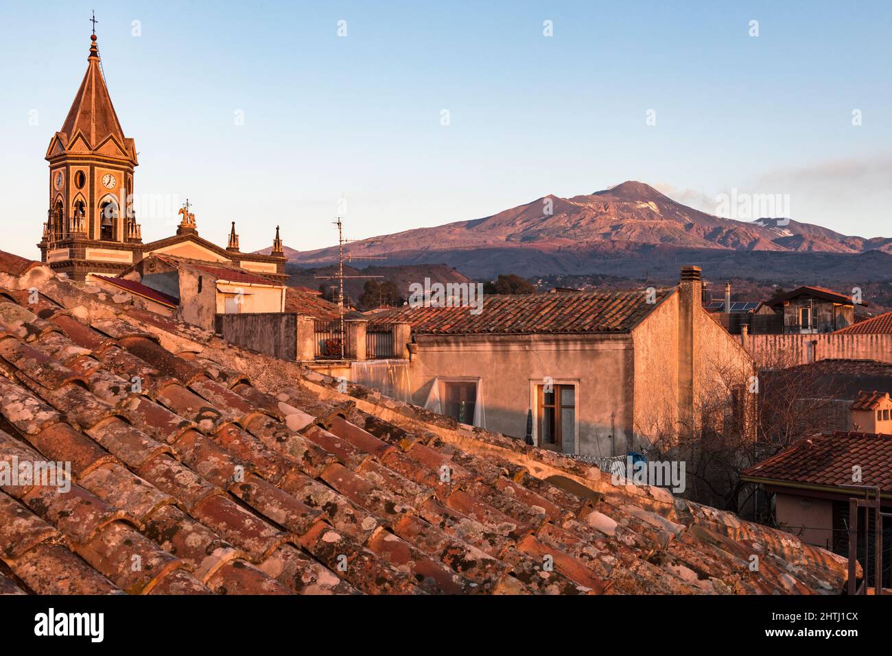 Mount Etna at sunrise, seen over the tiled roofs of the small town of Trecastagni on the southern slope of the volcano (Sicily, Italy) Stock Photo