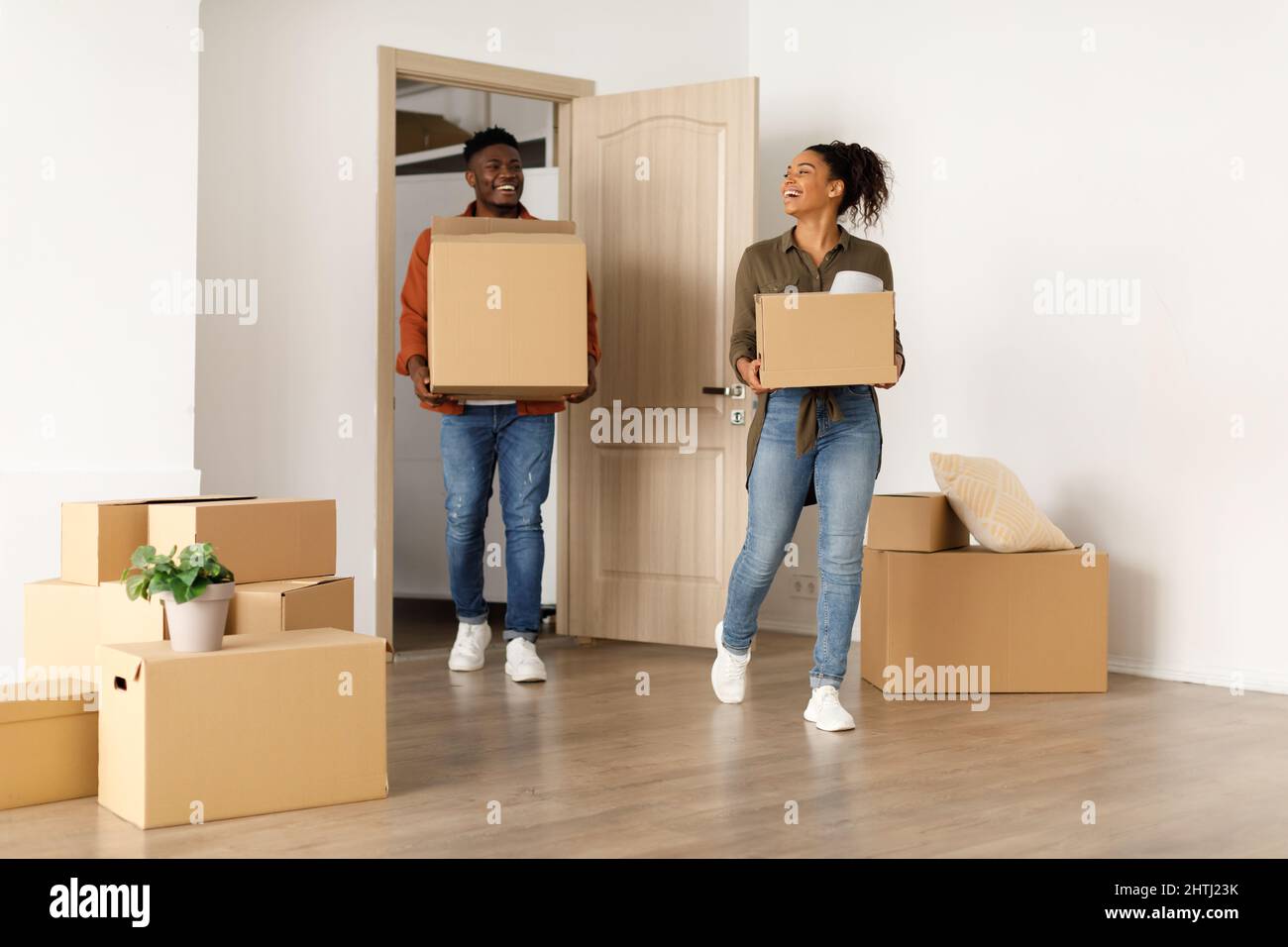 Happy Black Couple Entering New Home Carrying Cardboard Boxes Indoors Stock Photo