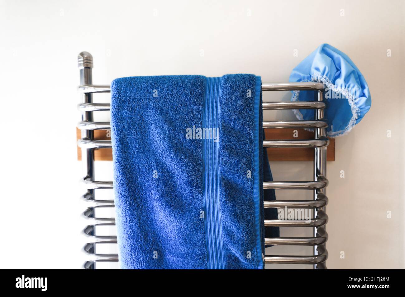 Blue towel and shower cap, hanging on a chrome ladder radiator. Stock Photo