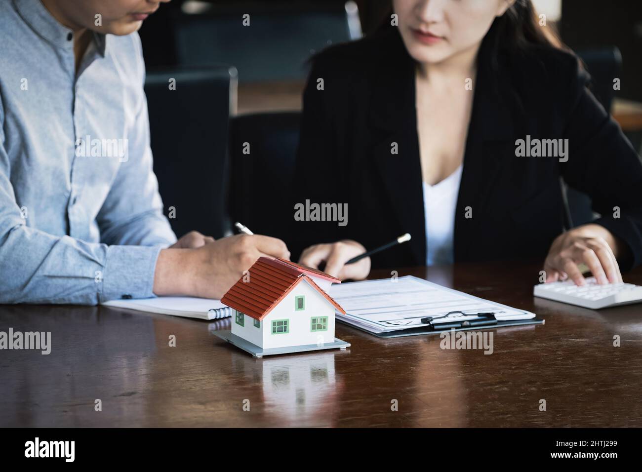 Concept of signing loan agreements, refinancing, buying and selling houses and land, focusing on model houses. A real estate agent is pointing to Stock Photo