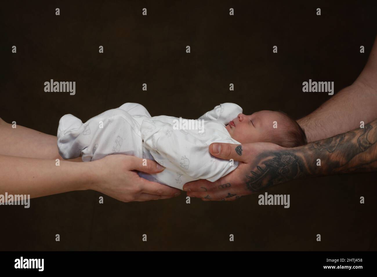 New born baby held safely by her parents strong secure hands. Stock Photo