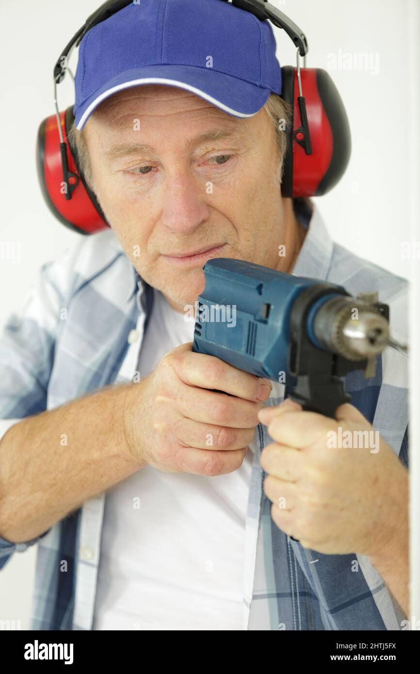 mature man using drill and wearing earmuffs Stock Photo