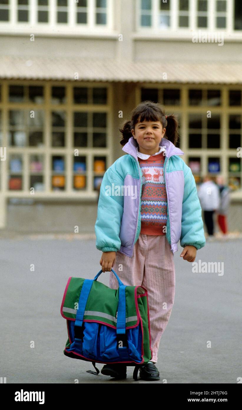 little girl front camera out of school carrying heavy satchel Stock Photo