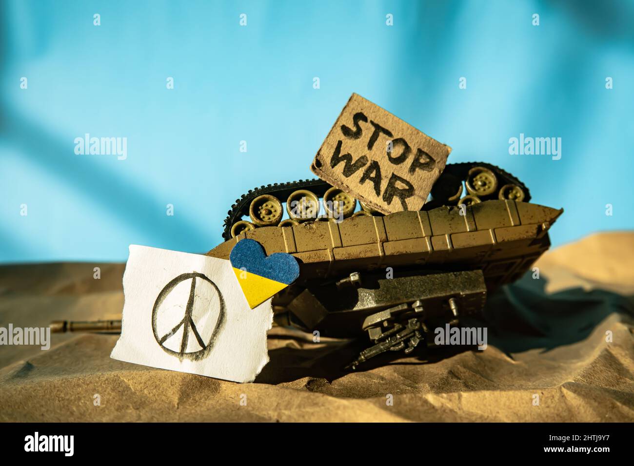 Overturned toy tank with peace symbol, Ukraine flag colored heart-shaped and stop war placard Stock Photo
