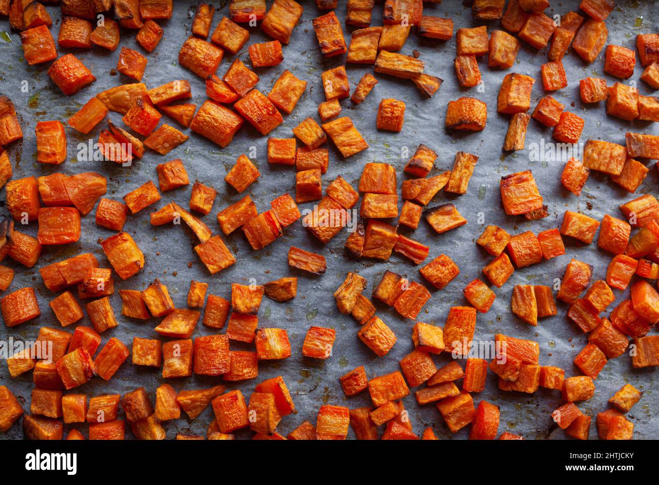 Oven roasted carrots and sweet potatoes on a parchment paper, cut into cubes Stock Photo