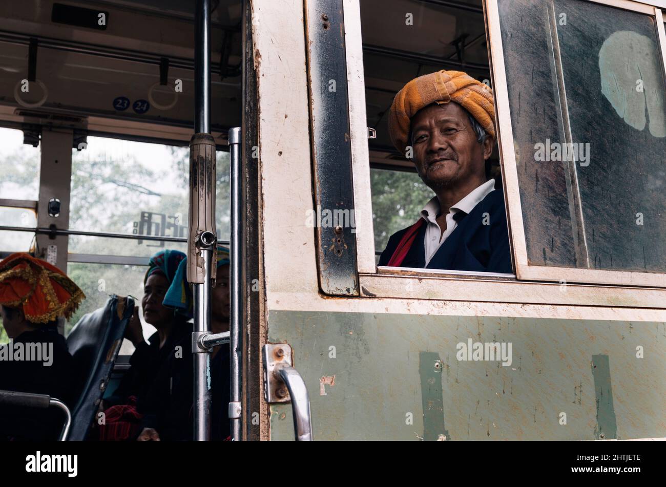 Kakku, Myanmar - 04.16.2017: Old Asian man from Karen ethnic minority with traditional towel turban near passengers in bus Stock Photo