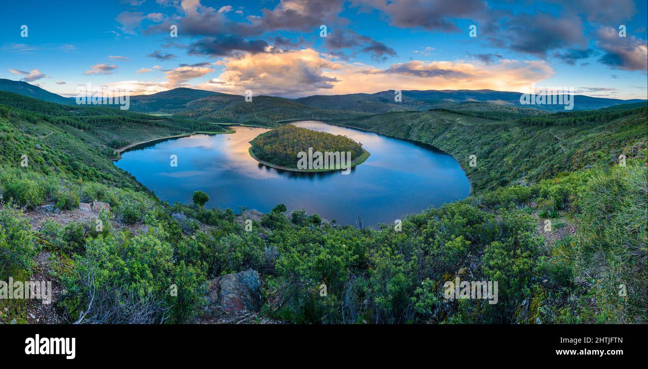 Breathtaking scenery of rainbow over calm river flowing through hilly terrain against cloudy blue sky in Meandro Del Melero National Park in Spain Stock Photo
