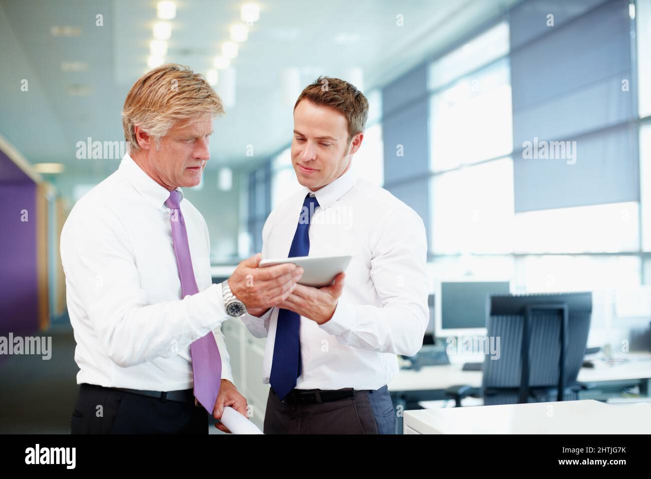Executives using tablet PC. Handsome business man with colleague using tablet PC in office. Stock Photo