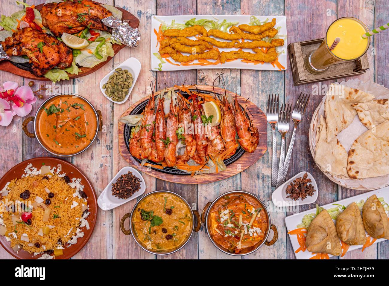 Set of Indian food dishes, beef samosas, prawn tikka, chicken tikka masala, korma, kashmiri pilau rice, garlic naan, mango lassi Stock Photo
